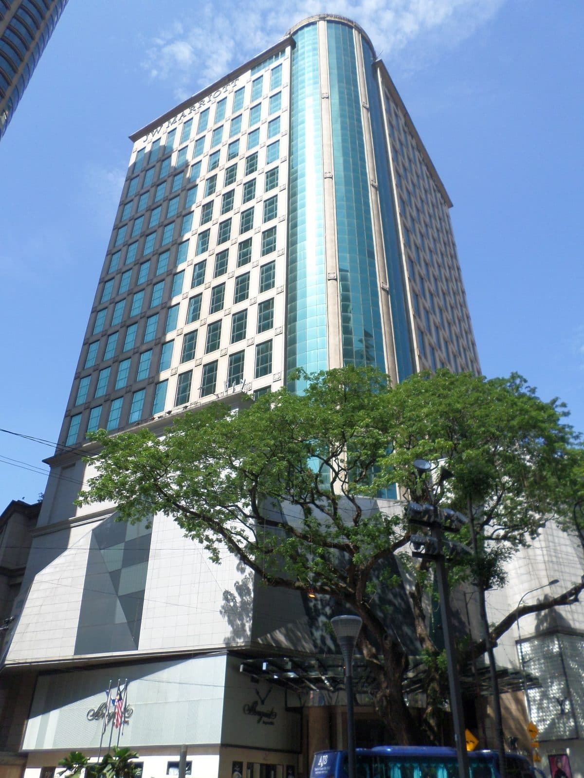 The JW Marriott Hotel Kuala Lumpur tower in Bukit Bintang, its name at the top, behind a large roadside tree